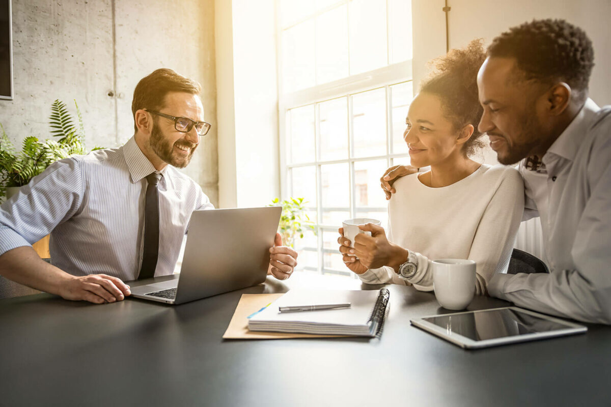 A couple sitting with a business professional that has his computer open.